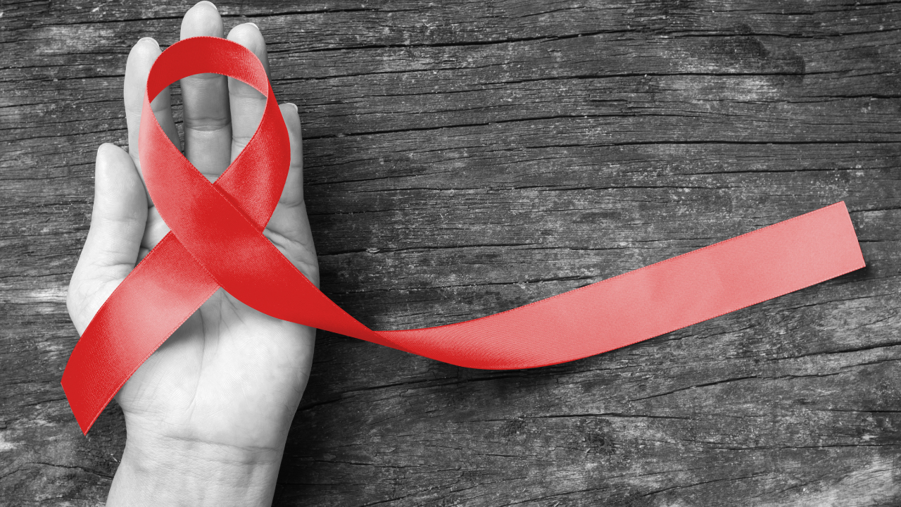 Red ribbon awareness on human hand with aged wood background with clipping path: World aids day: Symbolic concept for raising awareness campaign on people with HIV concept. Image Credit: Adobe Stock Images/Chinnapong